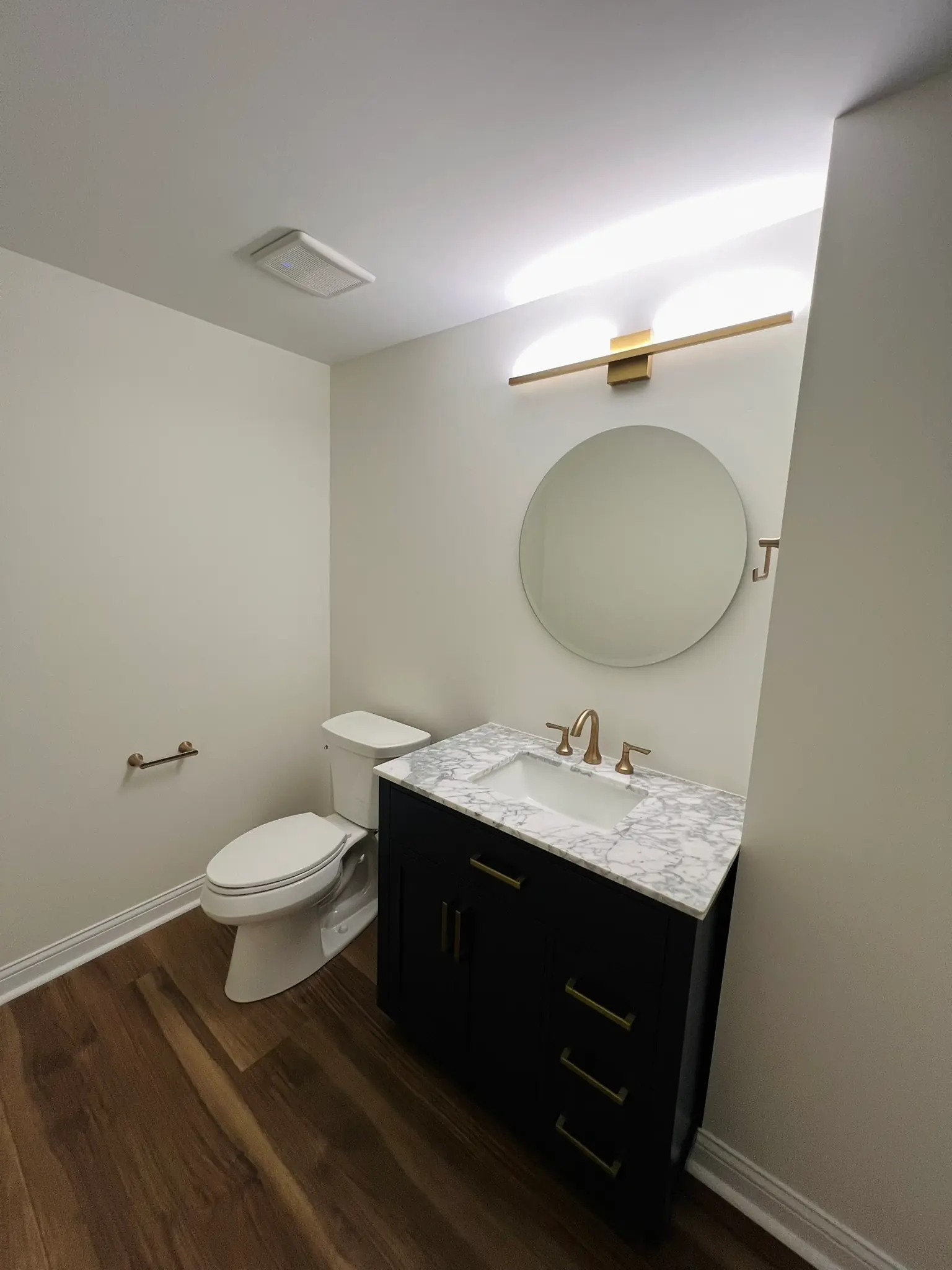 Basement bathroom with black vanity, marble countertop, round mirror, and gold fixtures