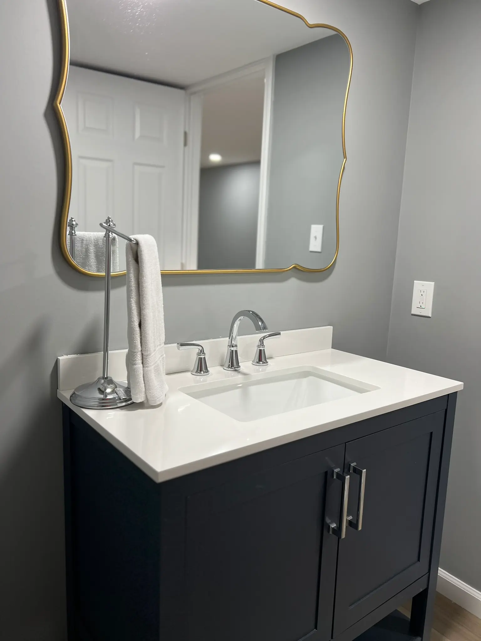 Basement bathroom navy vanity closeup with white quartz countertop, chrome faucet, and wavy gold mirror