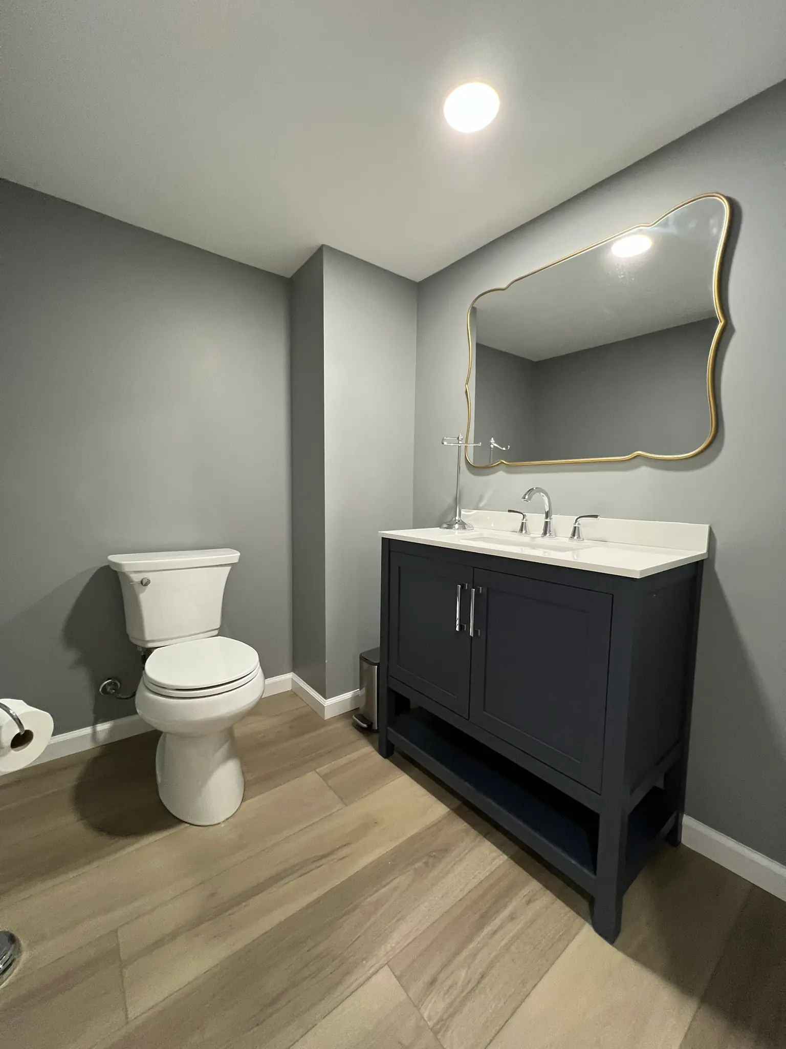 Basement half bathroom with navy vanity, white quartz countertop, gold-framed mirror, and chrome fixtures