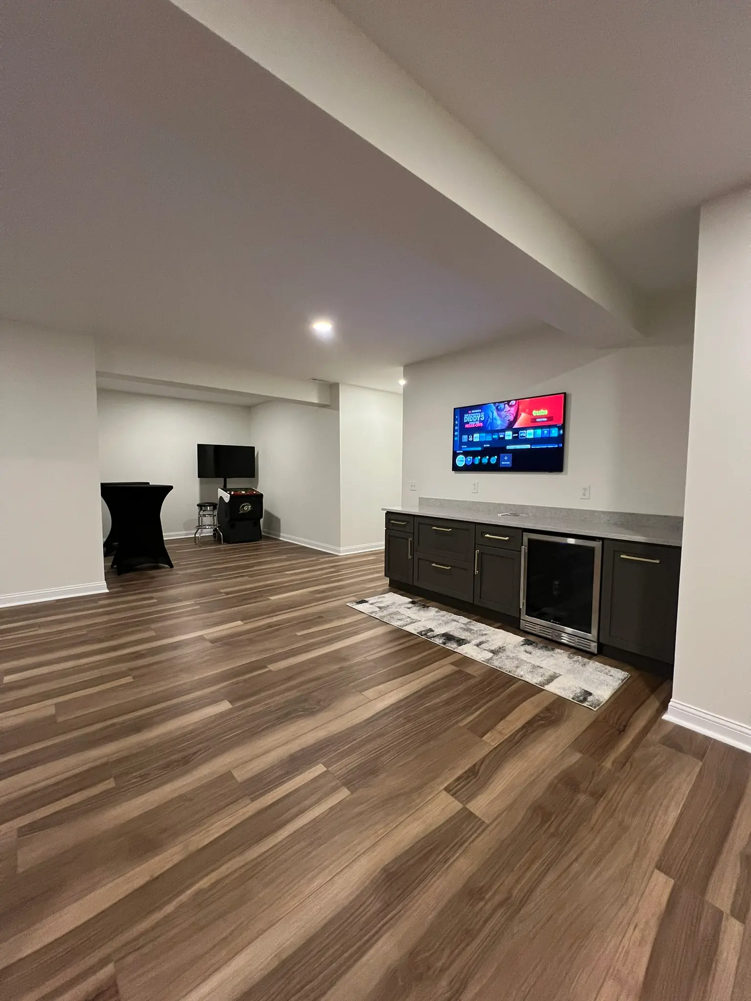 Finished basement entertainment area with dark wet bar, beverage fridge, and wall TV