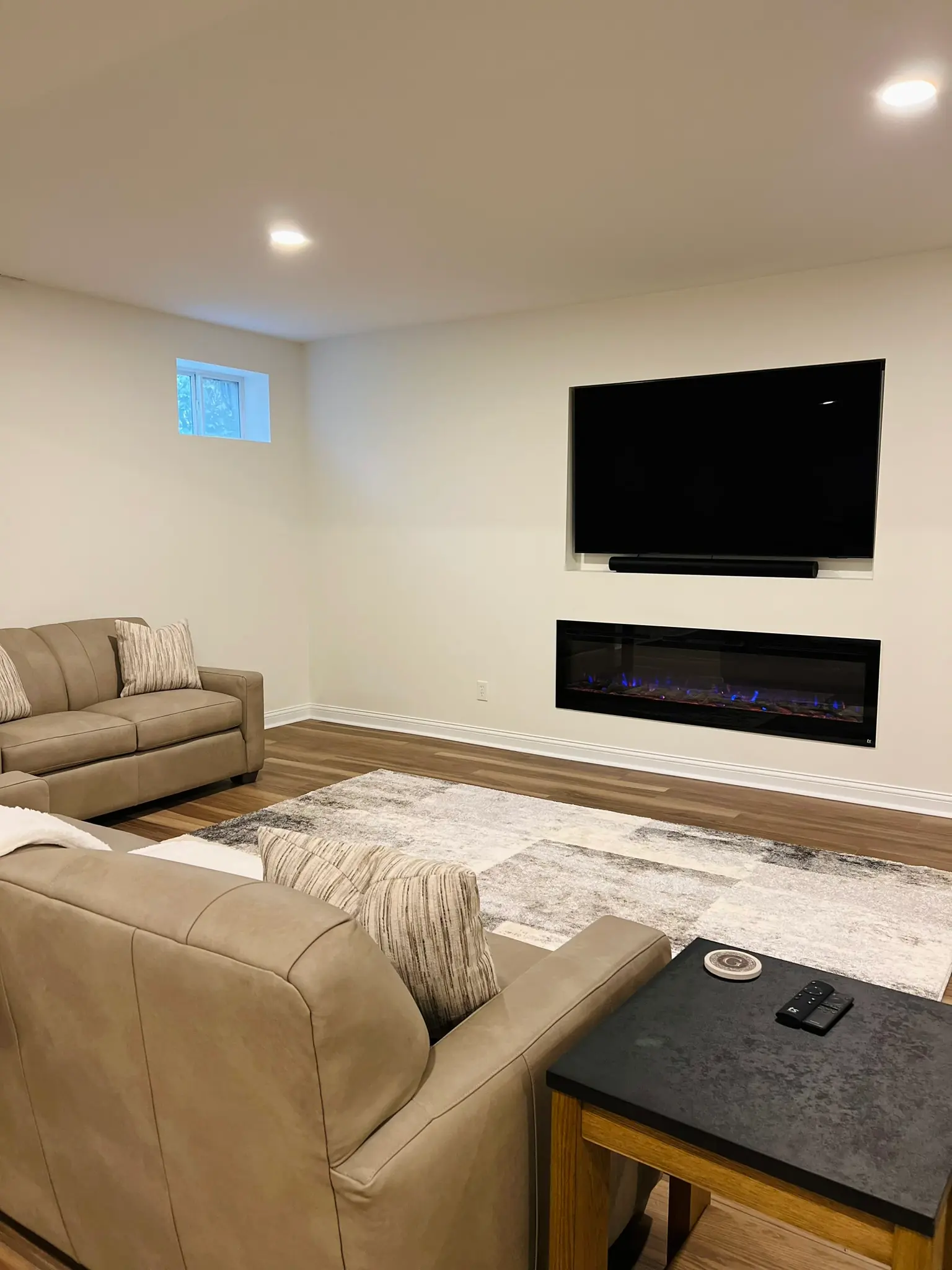 Finished basement family room with beige sofas, linear electric fireplace, and wall-mounted TV