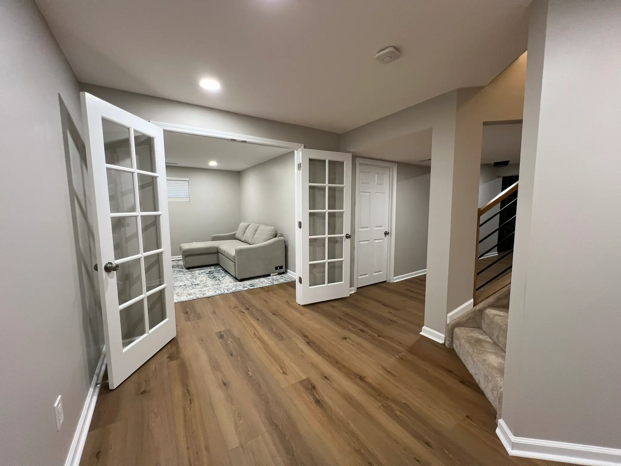Finished basement with French doors leading to media room with sectional sofa and hardwood LVP