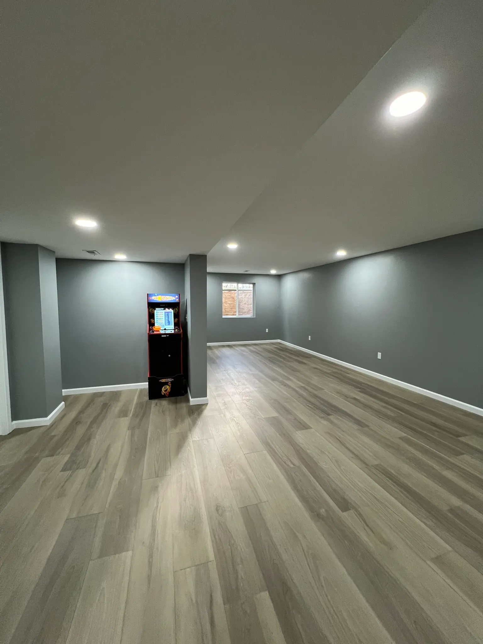 Finished basement game room with arcade cabinet, gray walls, LVP flooring, and recessed lighting