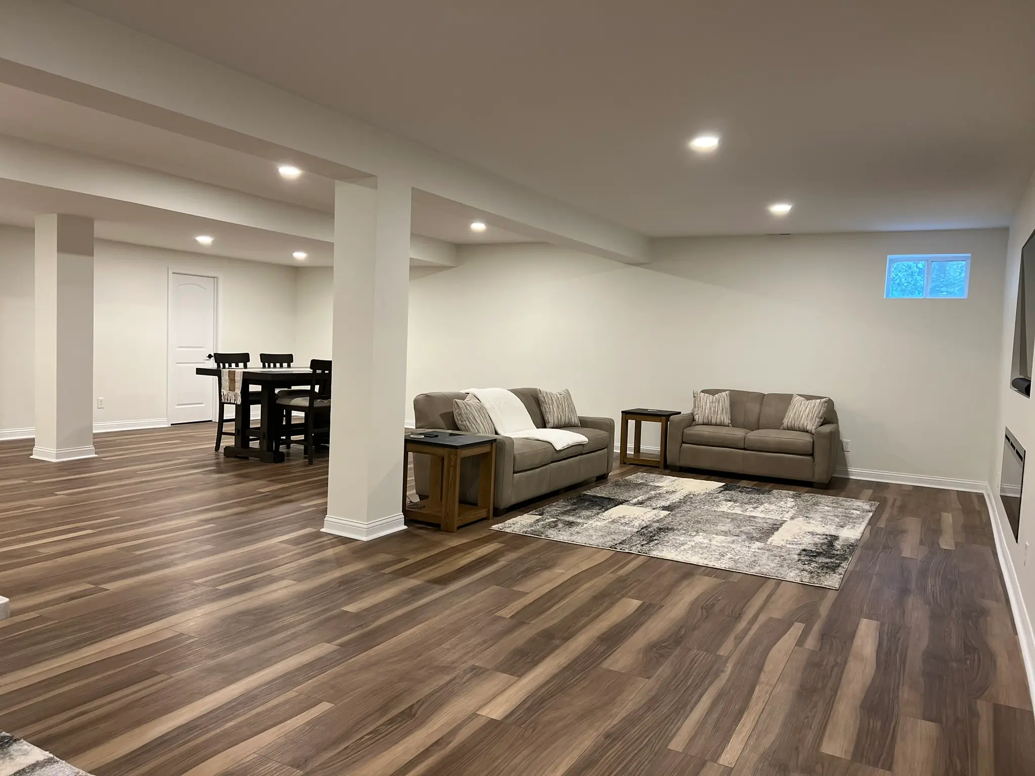 Finished basement with open concept layout, two sofas, area rug, and hardwood LVP flooring