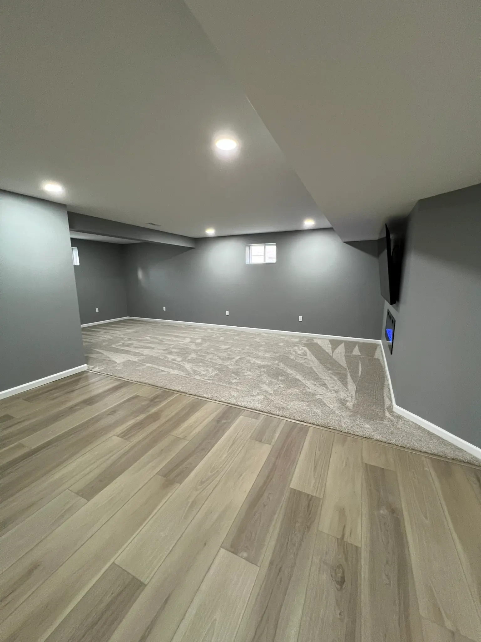 Finished basement open layout with gray walls, LVP and carpet flooring, and electric fireplace