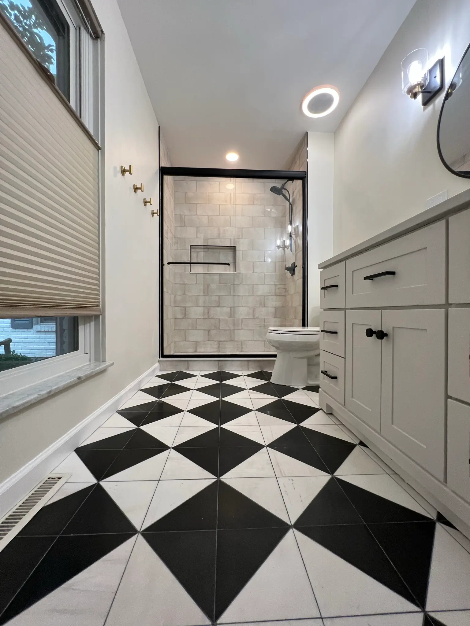 Full bathroom remodel with bold black-and-white diamond floor tile, black-trim shower, and white shaker vanity