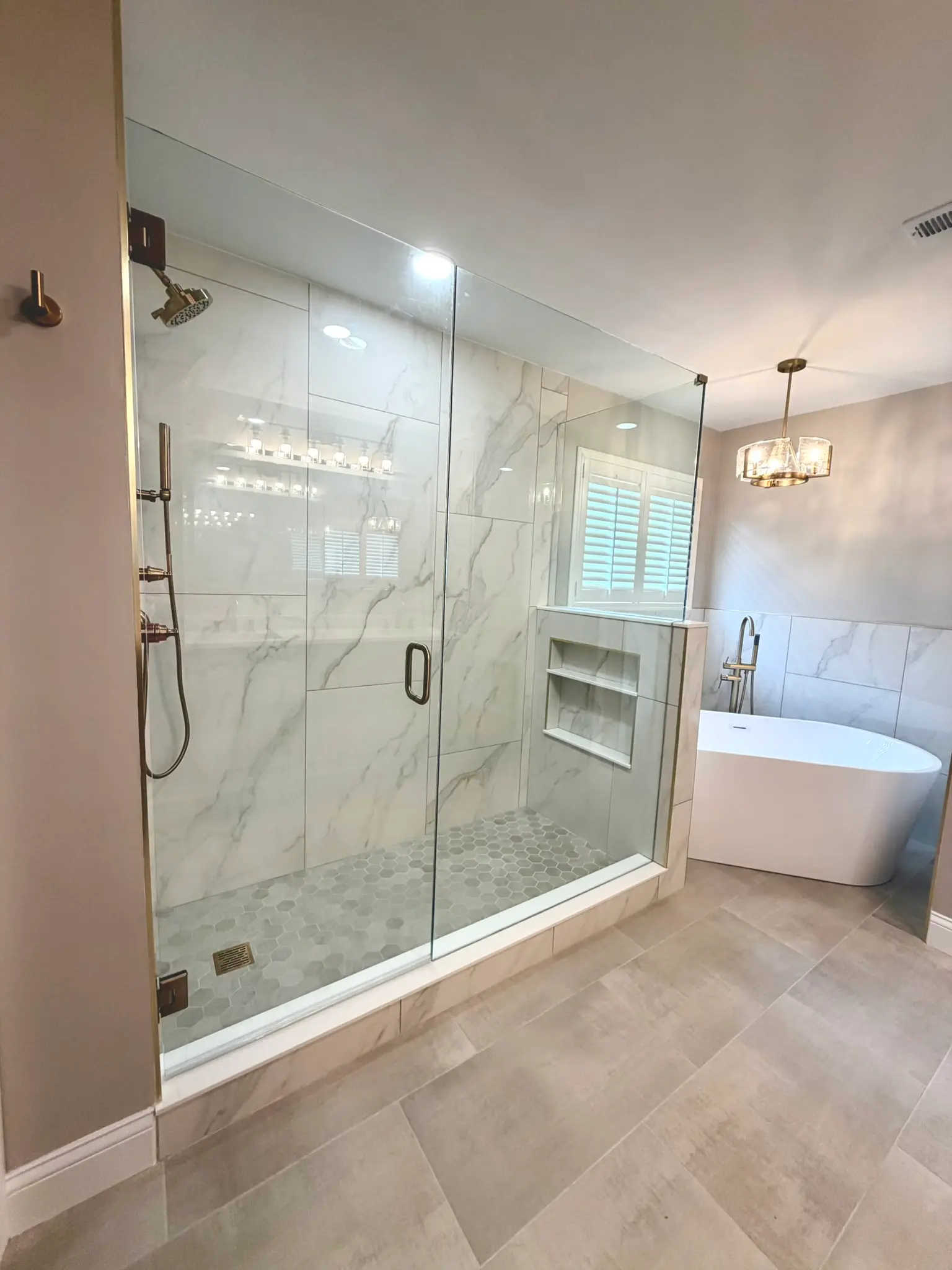 Frameless glass shower enclosure with marble-look tile, gold fixtures, and adjacent freestanding tub