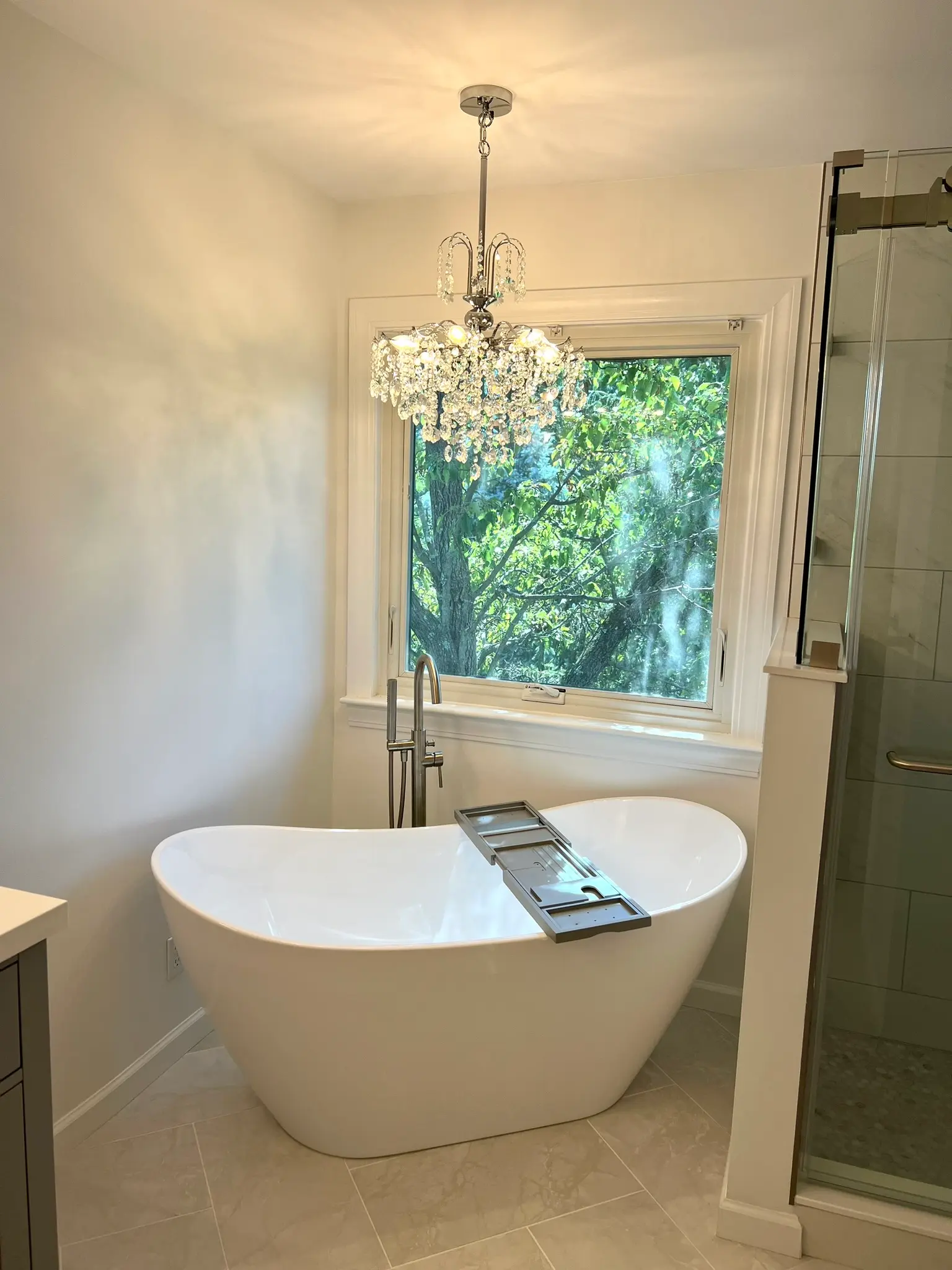 Freestanding soaking tub below crystal chandelier with frameless glass shower