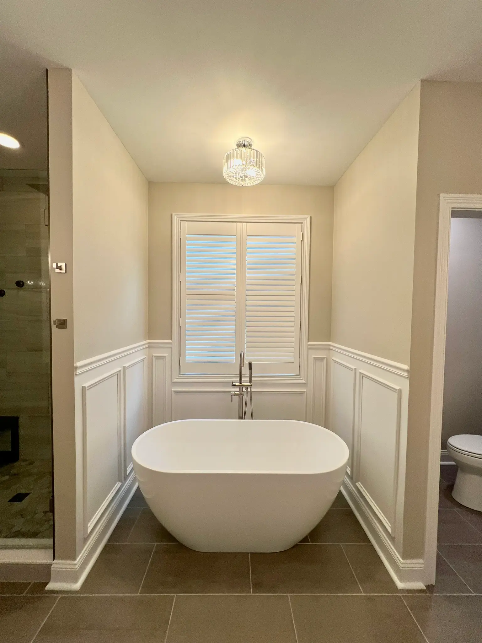 Freestanding soaking tub in custom nook with board-and-batten wainscoting and plantation shutters