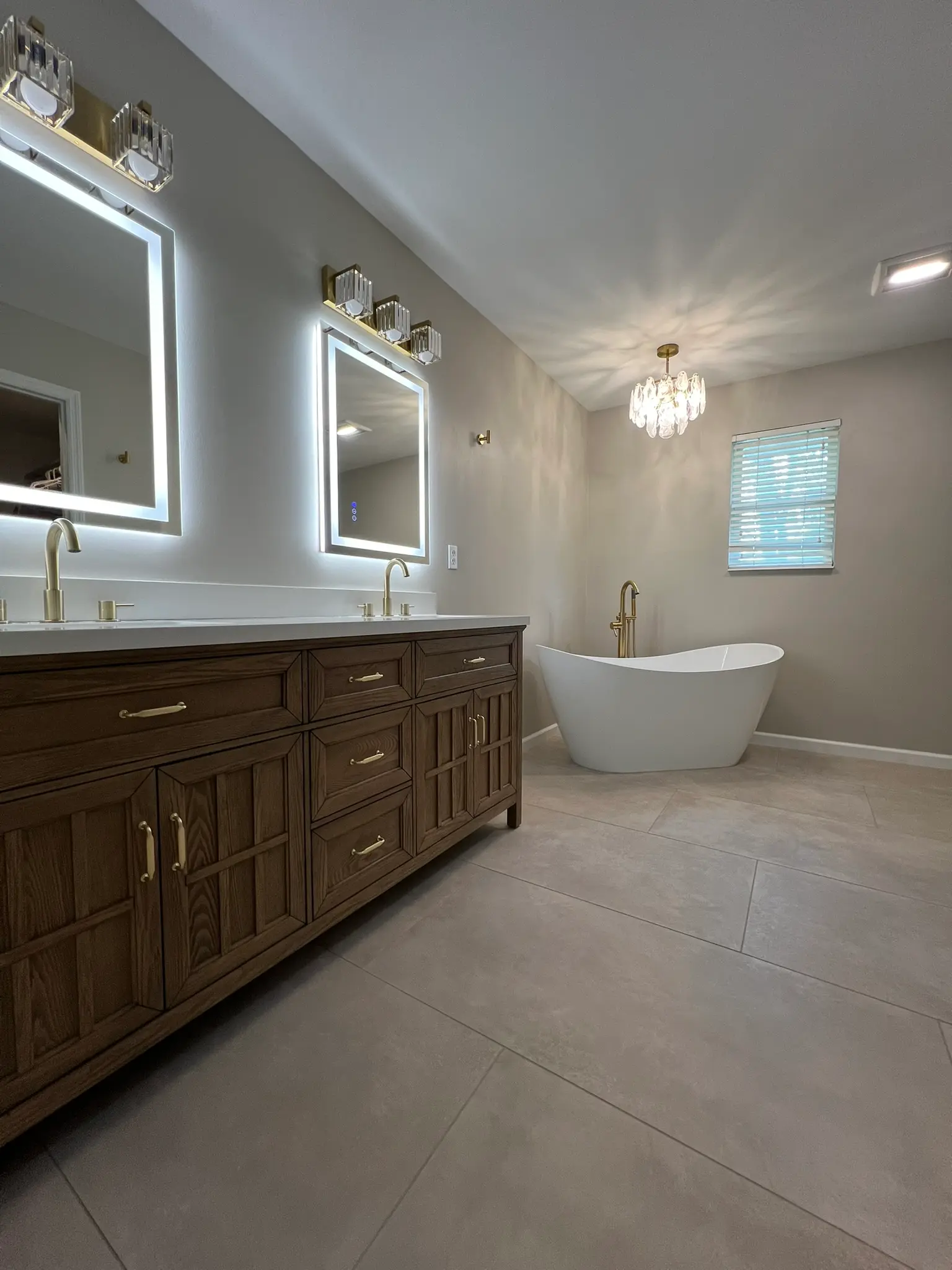 Primary bathroom with gold fixtures, dual LED mirrors, crystal chandelier, and freestanding soaking tub