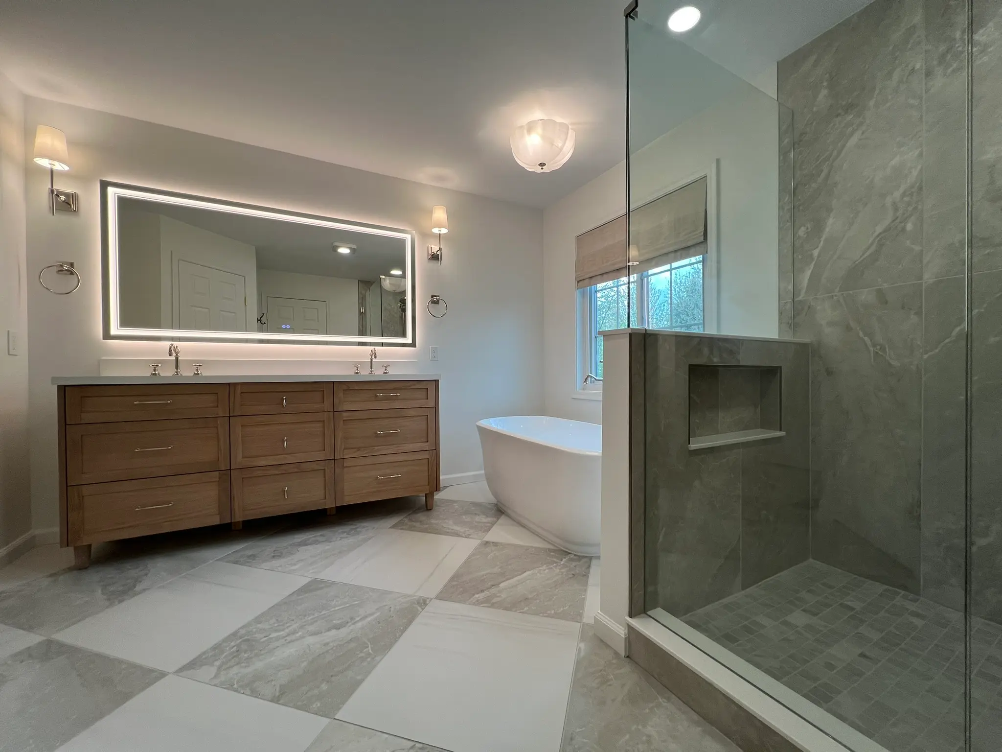 Primary bathroom remodel with wood double vanity, LED backlit mirror, freestanding soaking tub, and marble-look tile floor by R.E.P. General Contracting