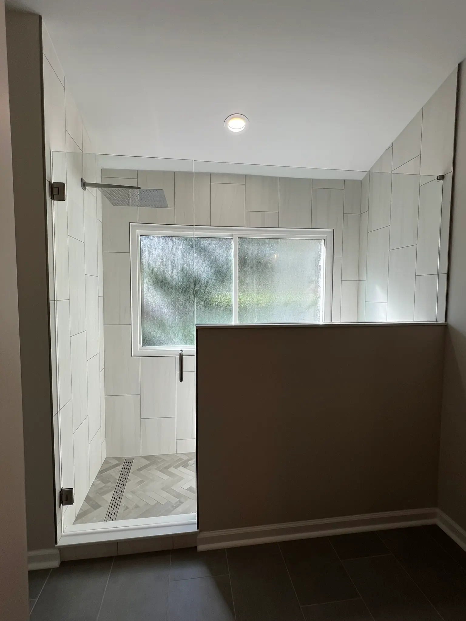 Walk-in shower with vertical white tile, herringbone mosaic floor, and frameless glass door