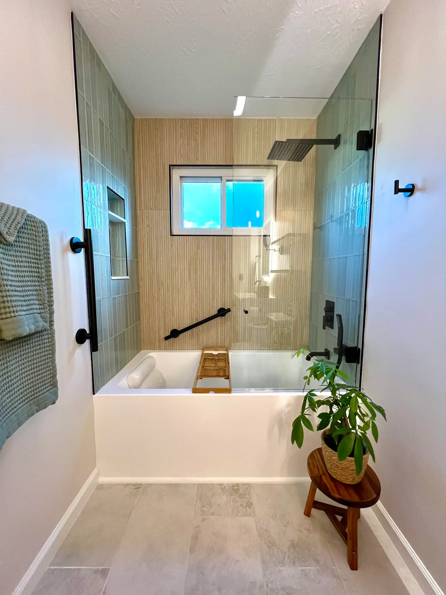 Tub-shower combo with green bamboo-look tile, black fixtures, and frameless glass enclosure