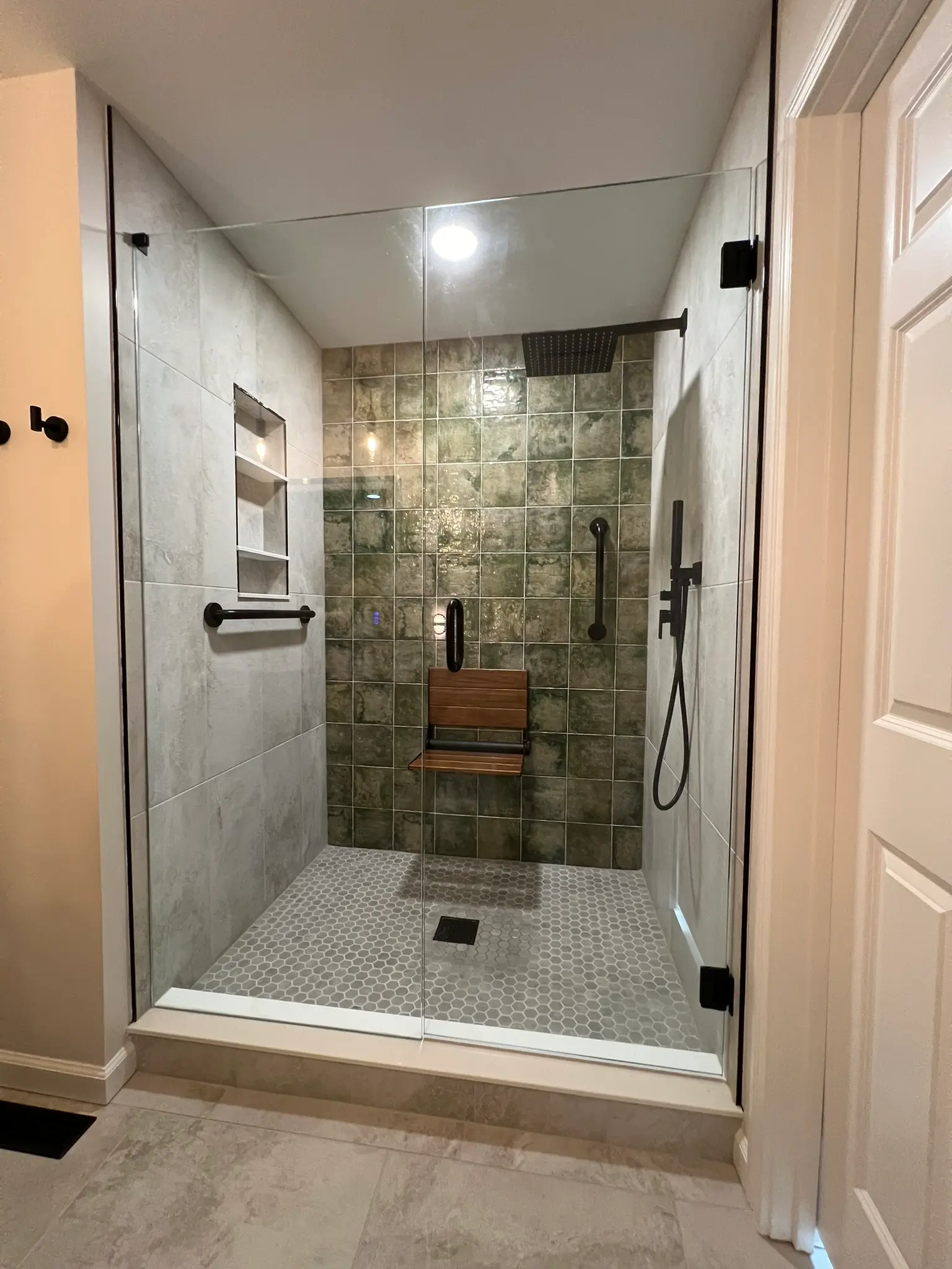 Walk-in shower with green stone tile, built-in teak bench, and rain showerhead