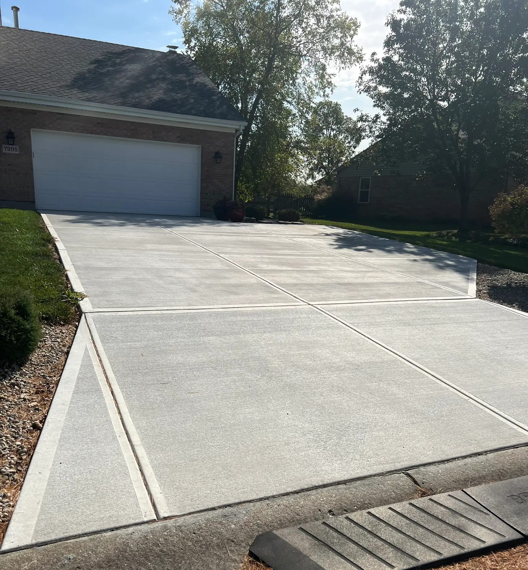 Full concrete driveway replacement leading to two-car garage on brick home