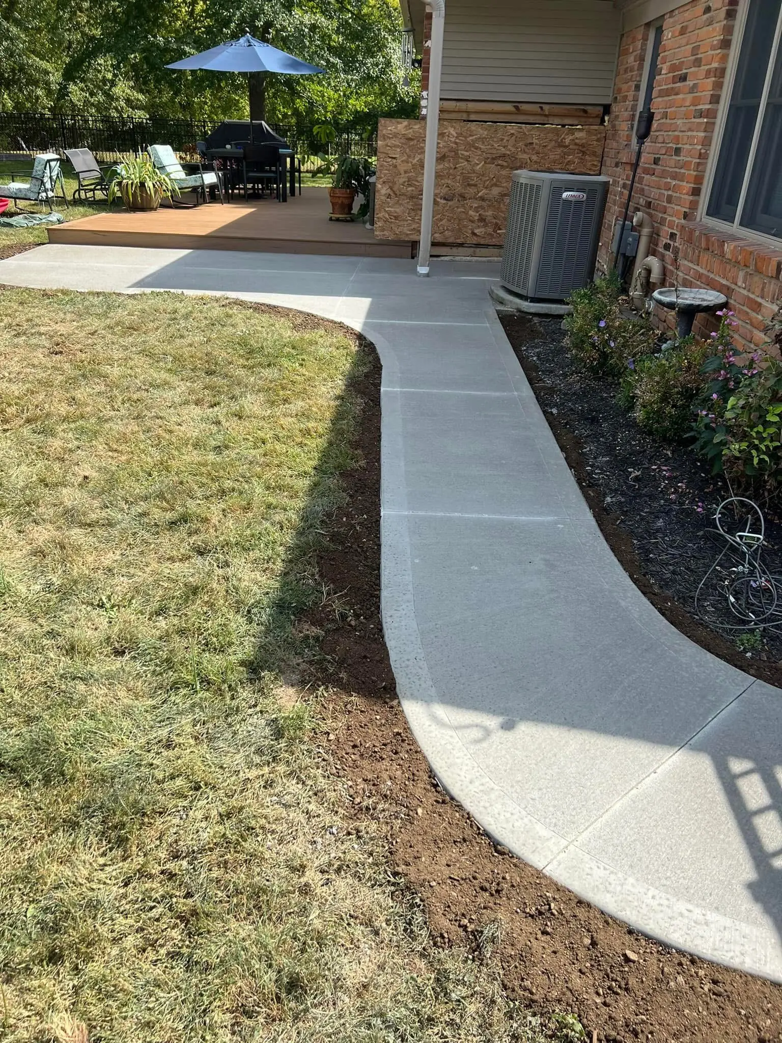 Curved concrete walkway connecting backyard patio area to yard