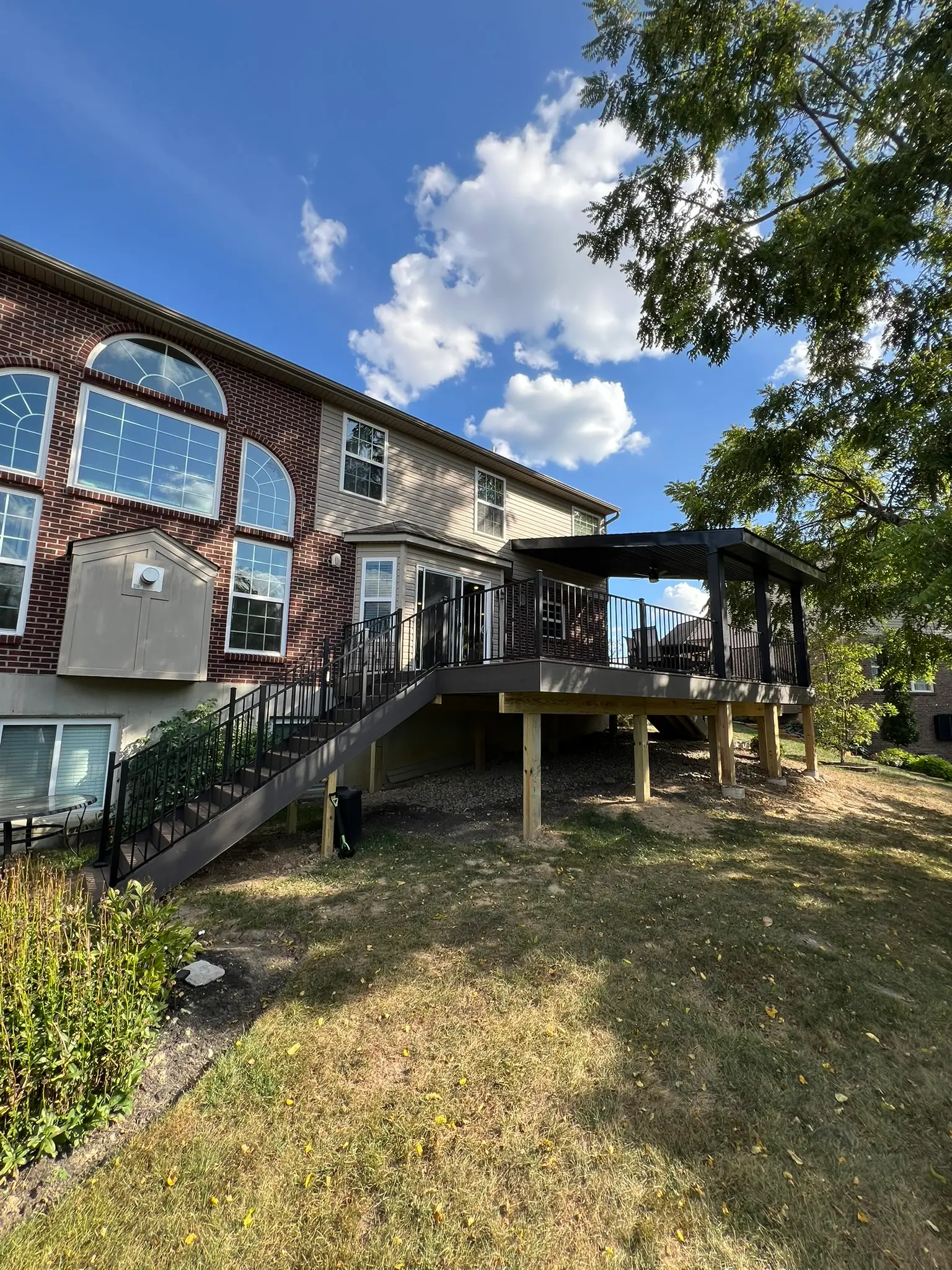 Elevated multi-level deck with covered pergola section and black railing on brick home
