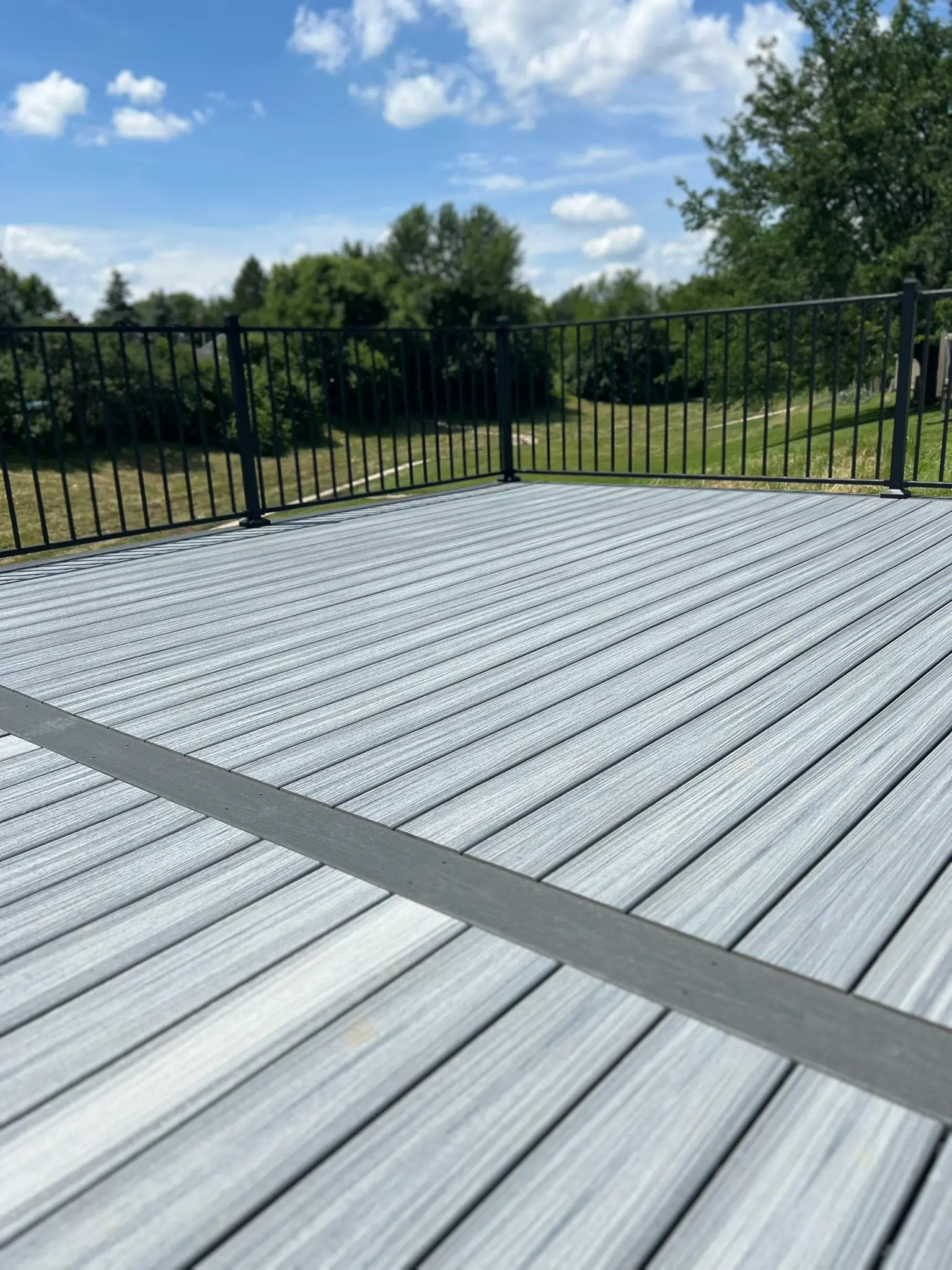 Gray composite deck surface with black railing and open backyard view