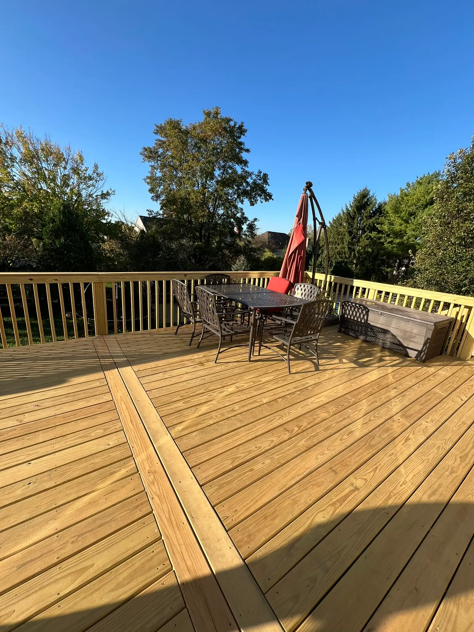Large pressure-treated wood deck with wood railing and outdoor dining set with umbrella