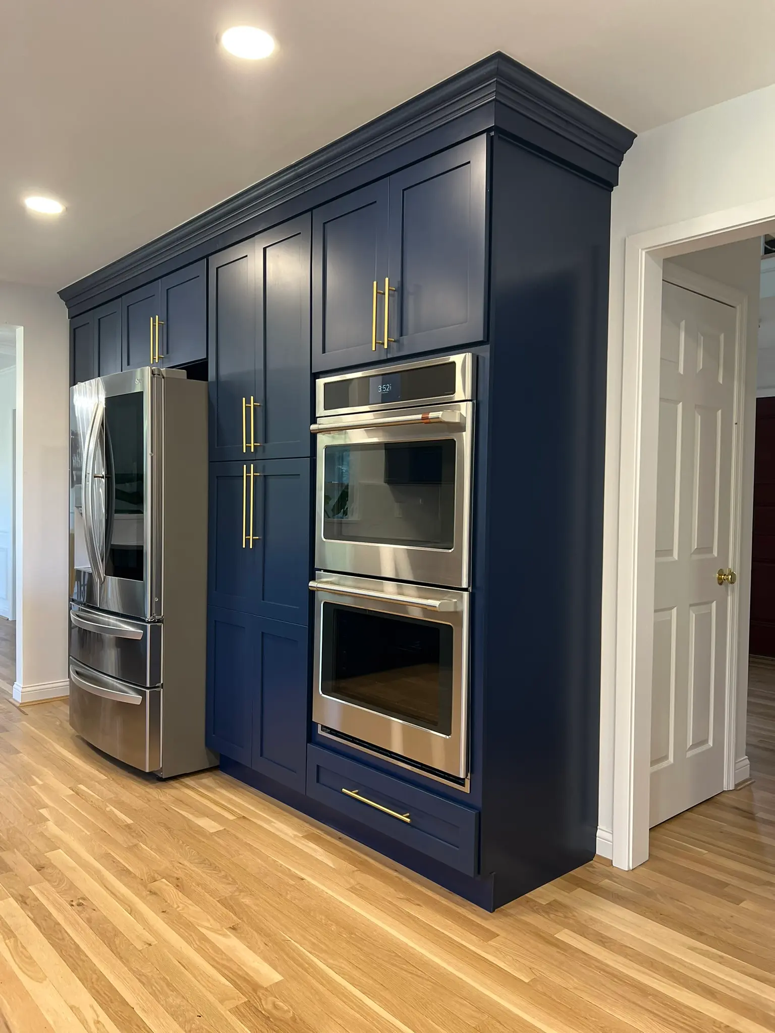 Navy blue floor-to-ceiling cabinetry with gold hardware, built-in double wall oven, and stainless French door refrigerator
