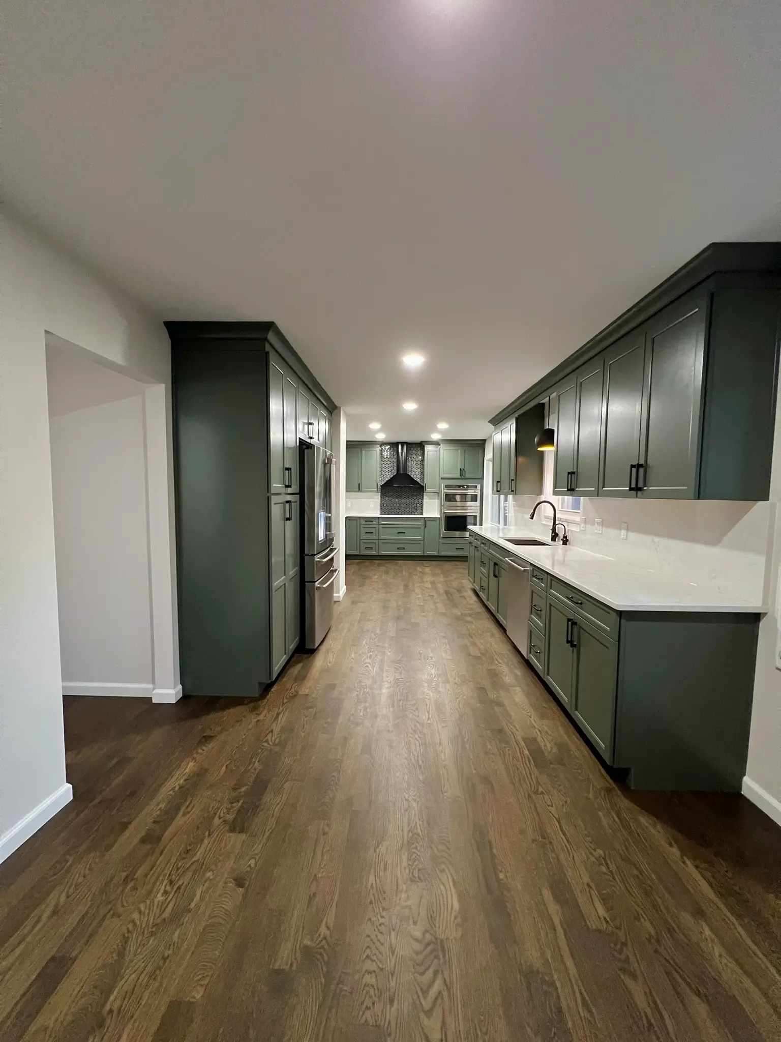 Expansive open-concept kitchen with sage green cabinets, black hardware, white quartz countertops, and dark hardwood floors