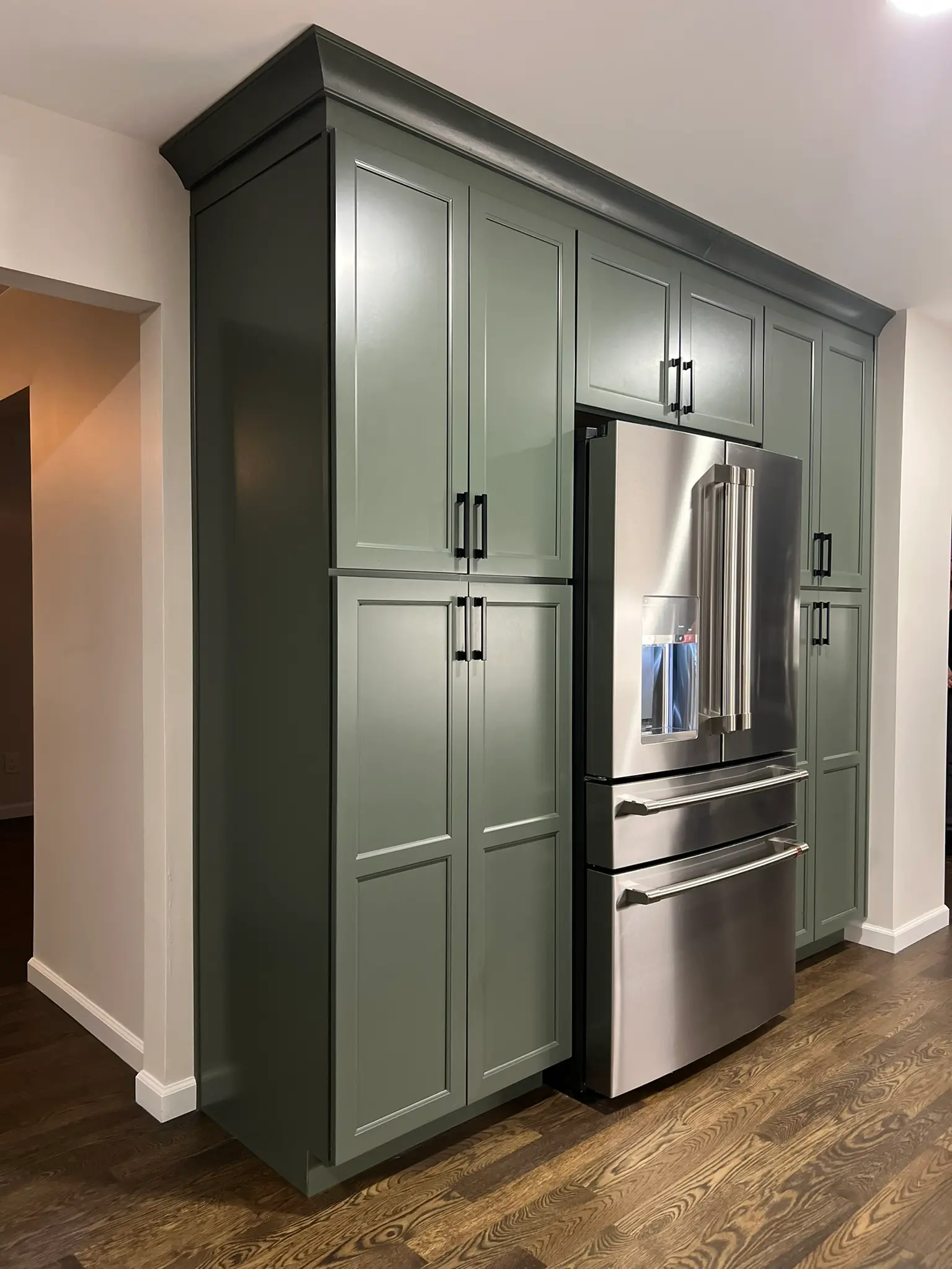 Sage green built-in pantry cabinet surround with integrated stainless French door refrigerator, black hardware, and crown molding detail