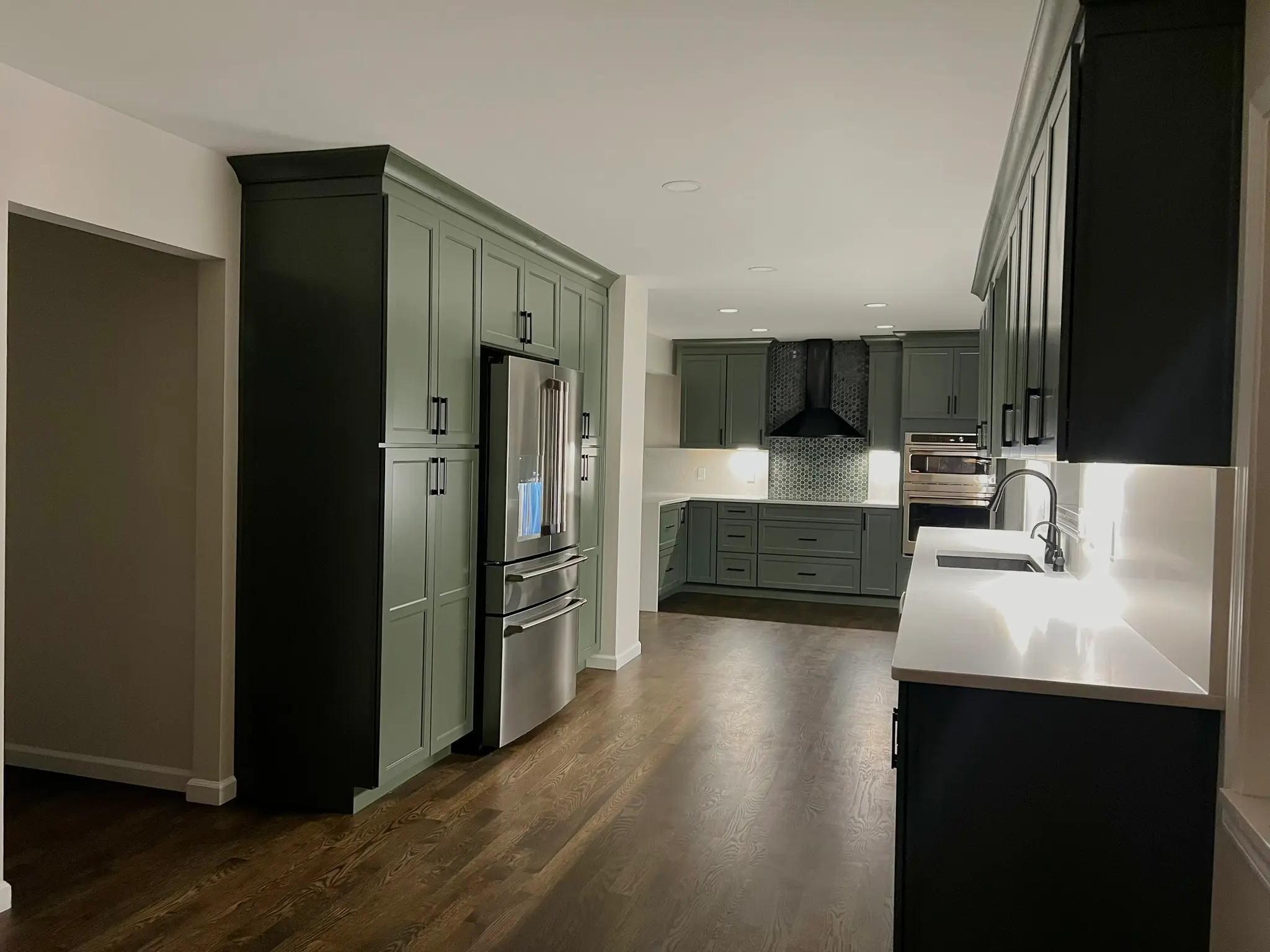 Two-tone kitchen with sage green pantry wall, dark island cabinetry, and white quartz countertops