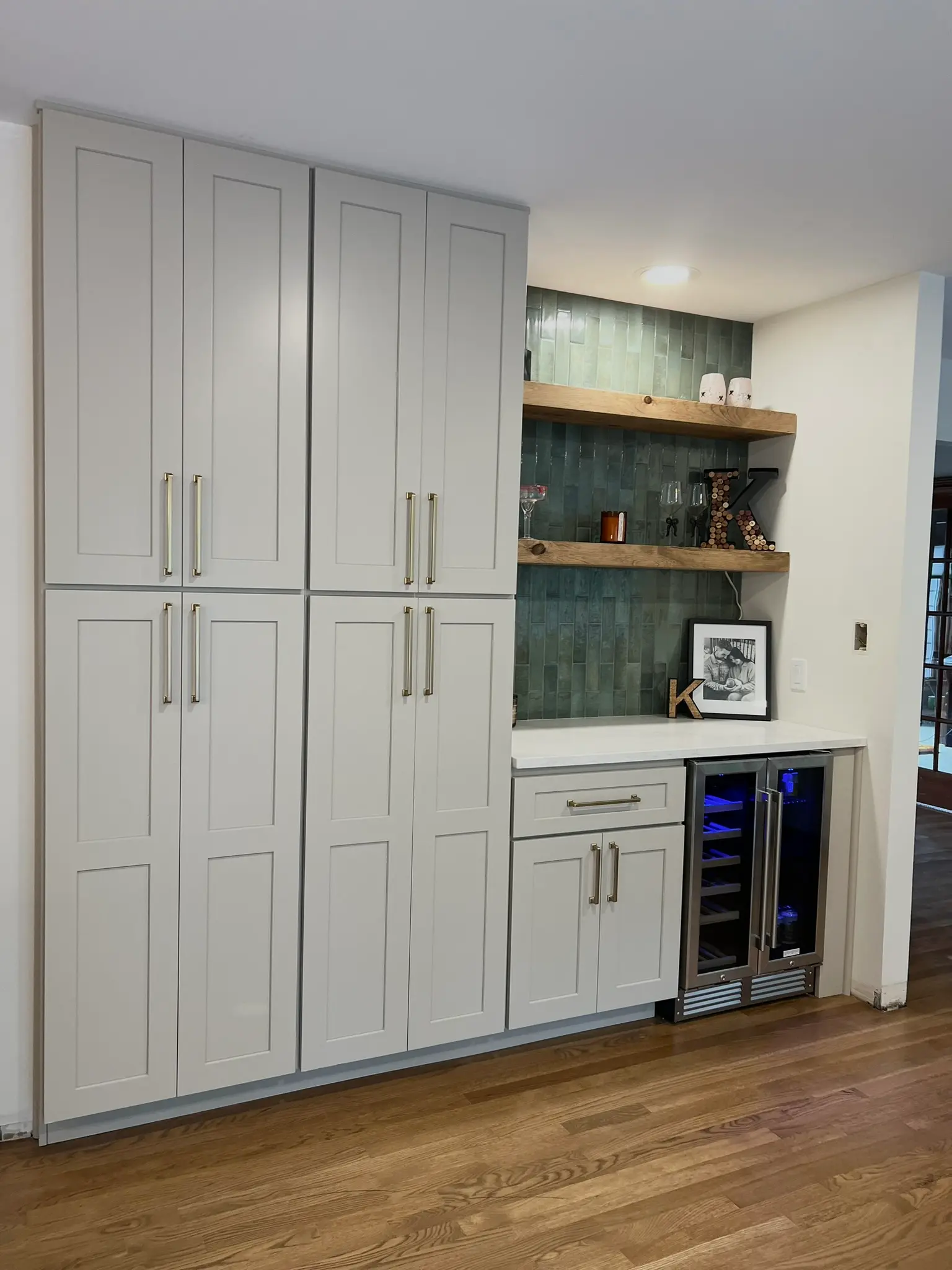 White kitchen with tall pantry cabinets, teal tile bar nook with built-in wine refrigerator and oak floating shelves